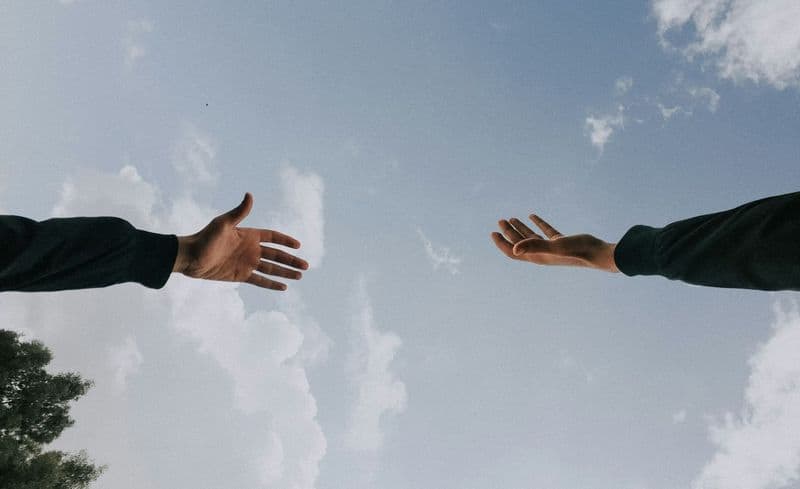 Due mani che si tendono l'una verso l'altra contro il cielo